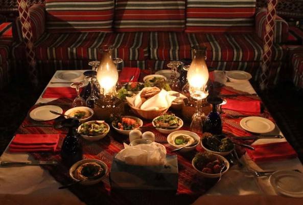 tourists enjoying belly dance, bbq dinner, tanoura and fire spinners on a bbq dinner in ras al khaimah desert